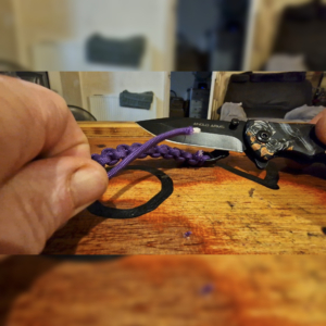 A photo of a pocket knife being safely used to trim the ends on a newly made paracord bracelet.
