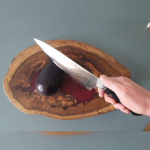 A photo of a Damascus Japanese knife cutting an abergine.